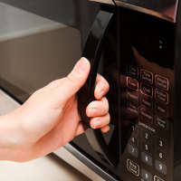 hand opening a microwave oven door to reheat pasta